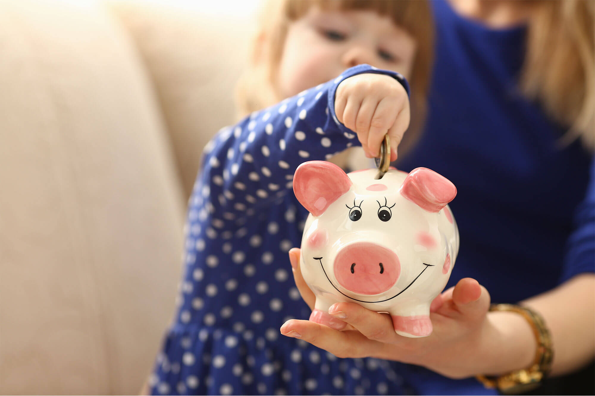 Young girl placing coins in piggy bank held by mother