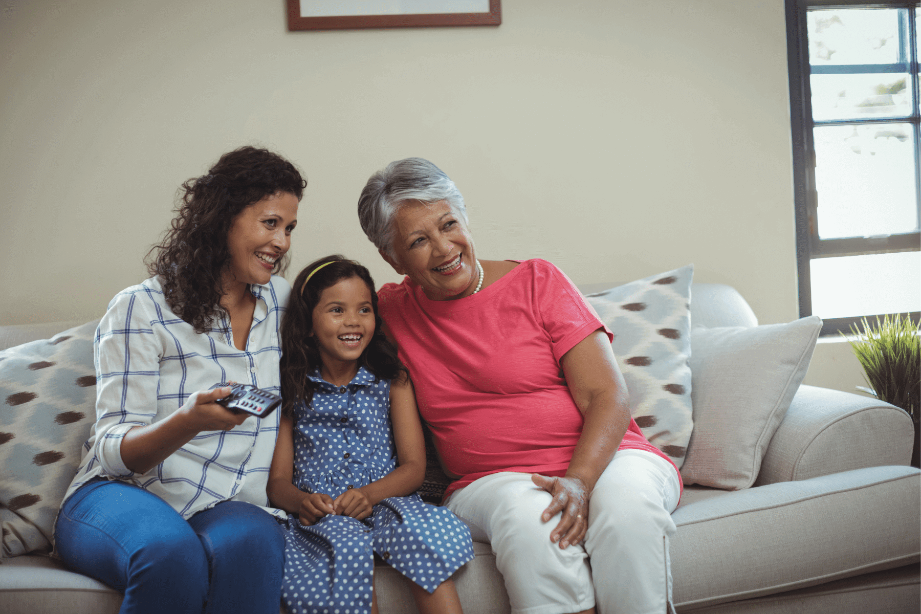 Grandmother, mother and daughter sitting on couch watching tv