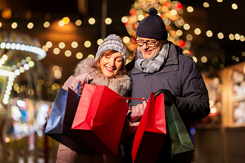Couple standing together holding shopping bags with Christmas tree behind them